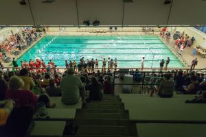 People sit in bleachers watching a swimming compeition.