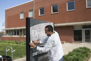 Man works on DMPS sign outside of brick building